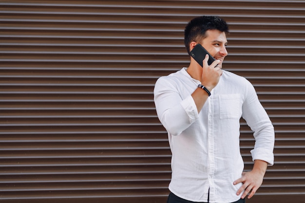 Young stylish guy in shirt talking by phone on simple 