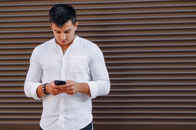 Young stylish guy in shirt typing on phone on simple 