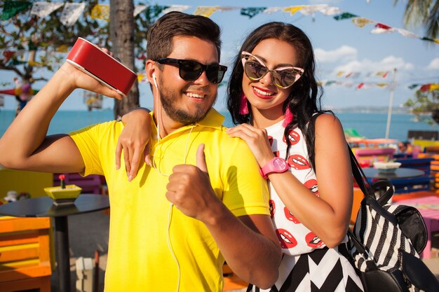 Young stylish hipster beautiful couple on summer vacation in Thailand, flirty, fashion trend outfit, sunglasses, tropical romance, smiling, happy, listening music, party mood, beach cafe