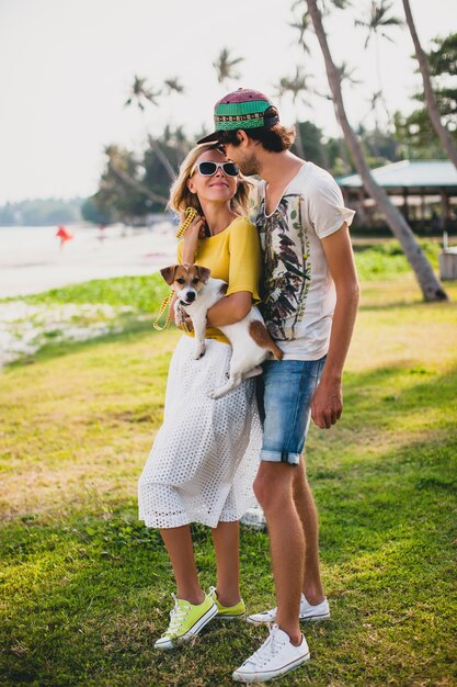 熱帯公園で犬を抱えて、笑顔で休暇中に楽しんで愛のスタイリッシュな流行に敏感な若いカップル