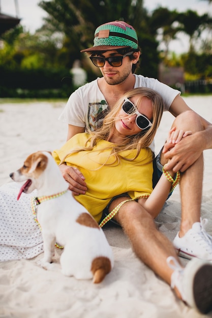 Young stylish hipster couple in love walking playing dog puppy jack russell, tropical beach, cool outfit, romantic mood, having fun, sunny, man woman together, horizontal, vacation, house home villa