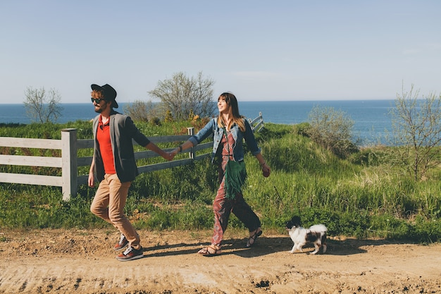 Young stylish hipster couple in love walking with dog in countryside, running, having fun