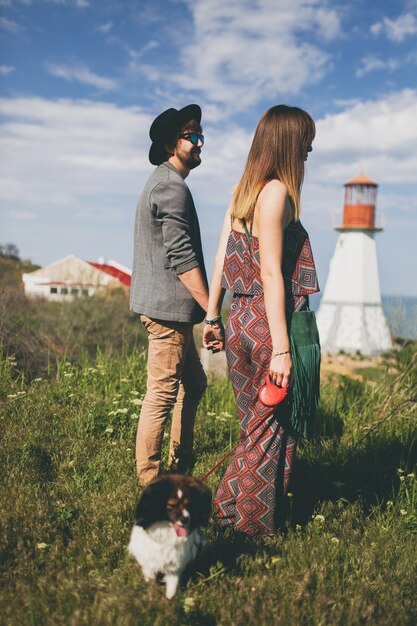 Young stylish hipster couple in love walking with dog in countryside