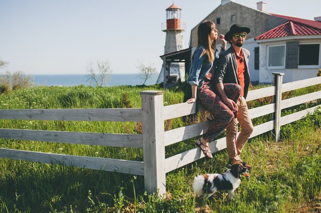 Young stylish hipster couple in love walking with dog in countryside