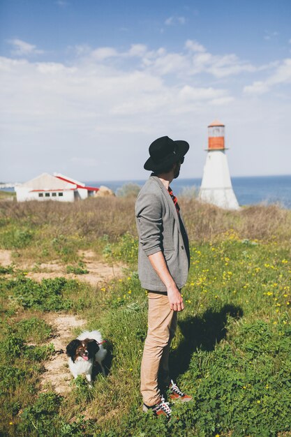 田舎で犬を連れて歩いて帽子のスタイリッシュな流行に敏感な若い男