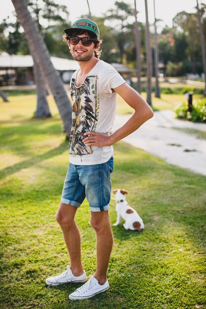 Молодой стильный хипстерский мужчина гуляет и играет с собакой на тропическом пляже