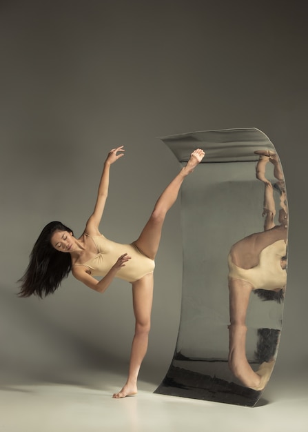 Young and stylish modern ballet dancer on brown wall with mirror. Illusion reflections on surface. Magic of flexibility, motion. Parallel dreamworld. Concept of creative art, action, inspiring.