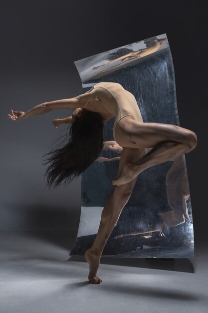 표면에 거울과 환상 반사와 회색 벽에 젊고 세련된 현대 발레 댄서