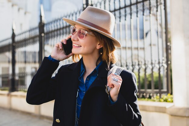 Young stylish pretty woman smiling, happy, surprised, talking on her phone, dressed in dark blue coat and denim shirt