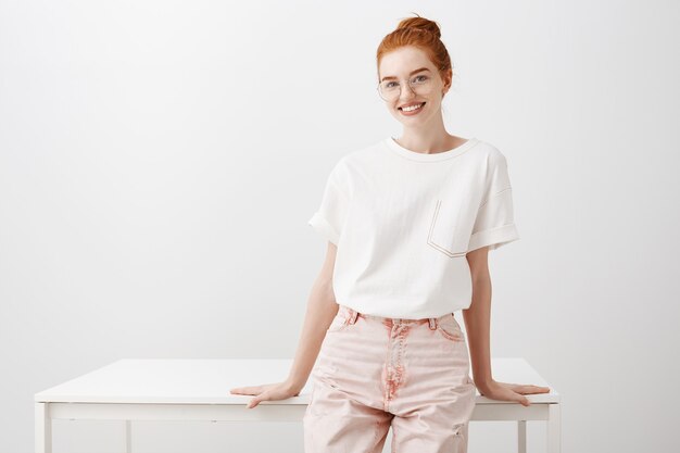 Young stylish redhead girl smiling, leaning on table