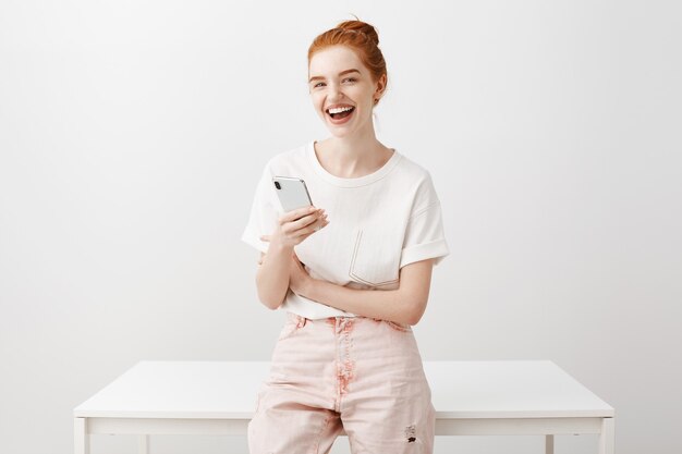 Молодая стильная рыжая девушка с помощью мобильного телефона разговаривает с кем-то и улыбается