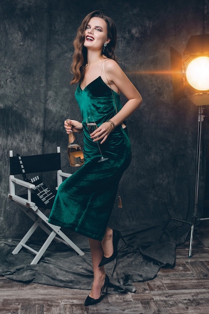 Foto gratuita giovane donna sexy alla moda sul cinema dietro le quinte, festeggia con un bicchiere di champagne