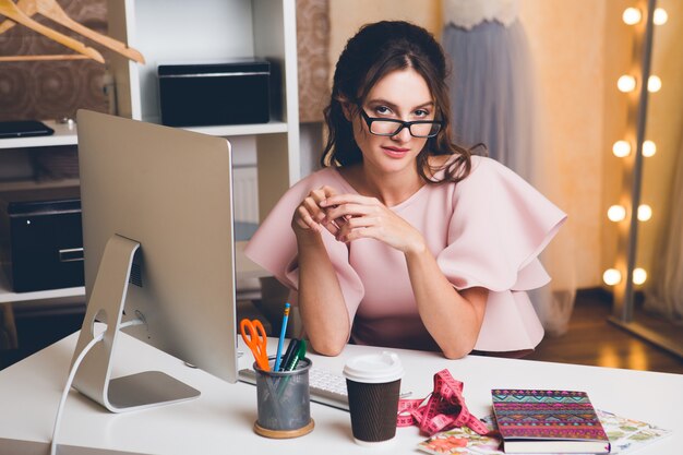 Young stylish sexy woman in pink luxury dress, summer trend, chic style, fashion designer working at office on computer