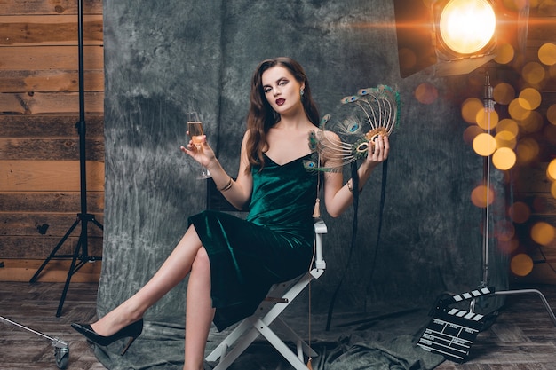 Молодая стильная сексуальная женщина, сидящая в кресле за кулисами кинотеатра, празднует с бокалом шампанского