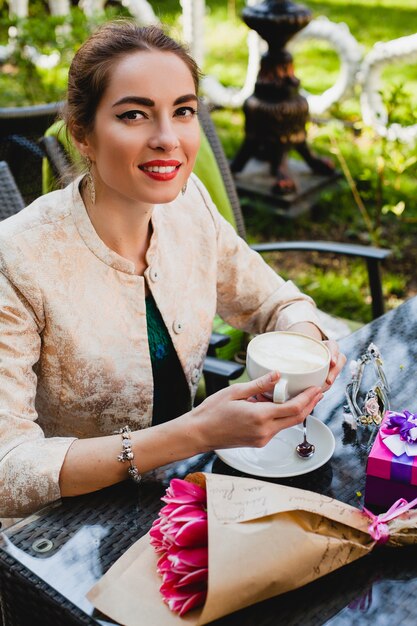 若いスタイリッシュな女性、ファッションサングラス、カフェに座って、カプチーノのカップを保持
