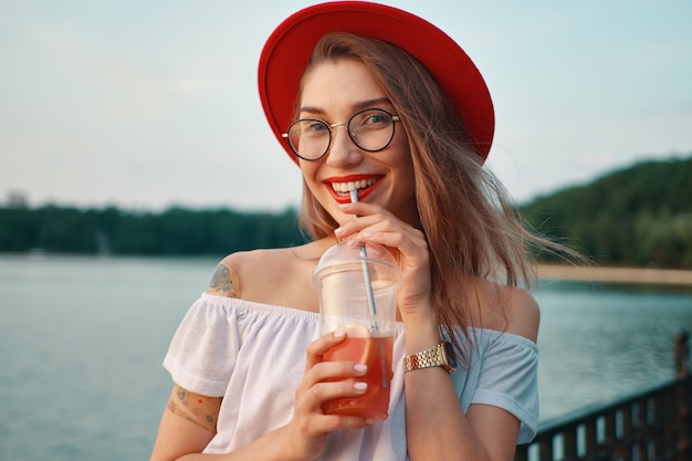 Foto gratuita una giovane donna alla moda con un drink rinfrescante mentre sorridente