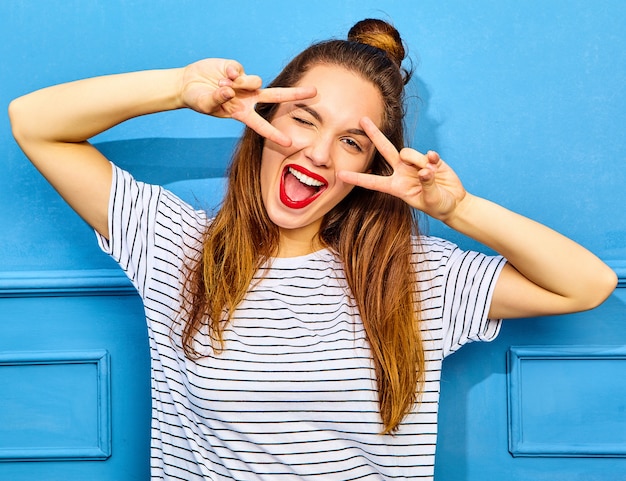 Free photo young stylish woman model in casual summer clothes with red lips, posing near blue wall. winking