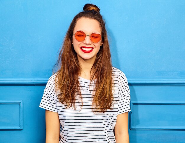 Young stylish woman model in casual summer clothes with red lips, posing near blue wall