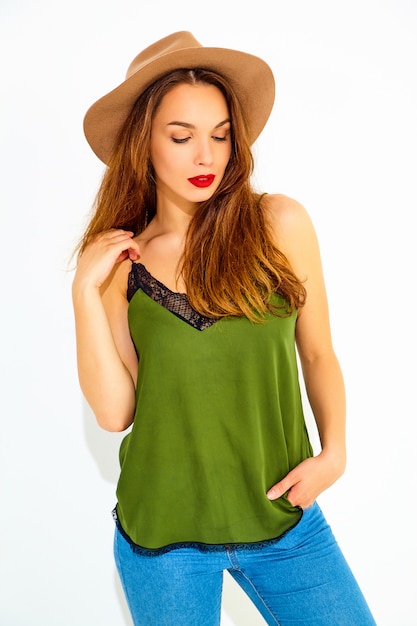 Young stylish woman model in casual summer green clothes and brown hat with red lips, posing near white wall