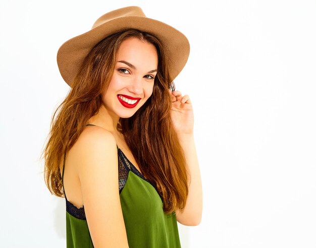 흰 벽 근처 포즈 캐주얼 여름 녹색 옷과 빨간 입술과 갈색 모자에 젊은 세련 된 여자 모델