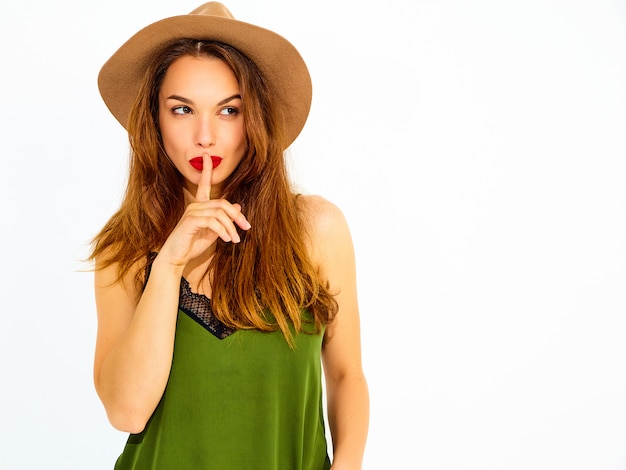 손가락으로 침묵 제스처를 보여주는 붉은 입술으로 캐주얼 여름 녹색 옷과 갈색 모자에 젊은 세련 된 여자 모델, 절연