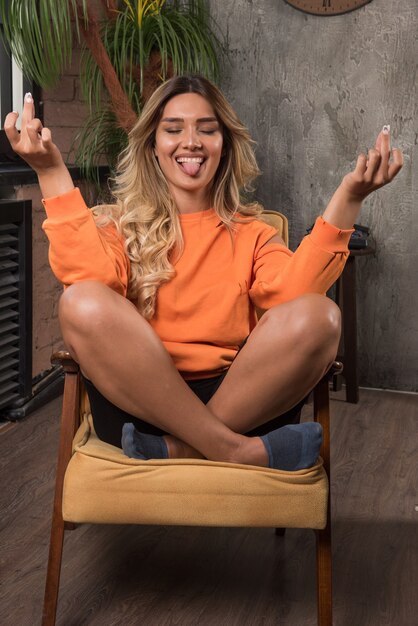 Young stylish woman sitting in armchair closing her eyes and making signs.