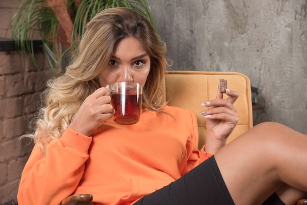 Young stylish woman sitting in armchair drinking cup of tea.
