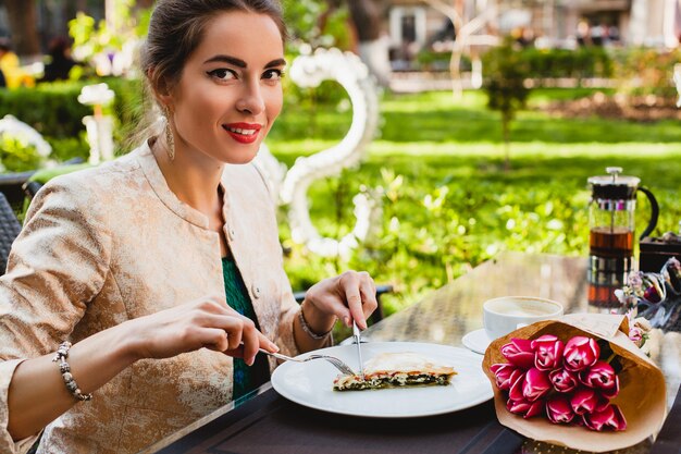 Giovane donna alla moda che si siede nella caffetteria, mangiando una gustosa torta