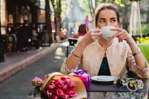 Free photo young stylish woman sitting in cafe, holding cup of cappuccino