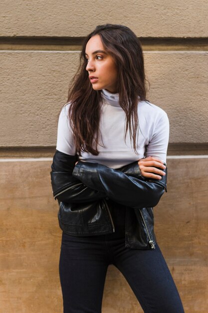 Young stylish woman standing against wall with her arms crossed