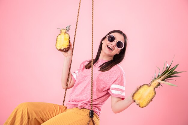 A young stylish woman in a summer look rides on swing on pink isolated.