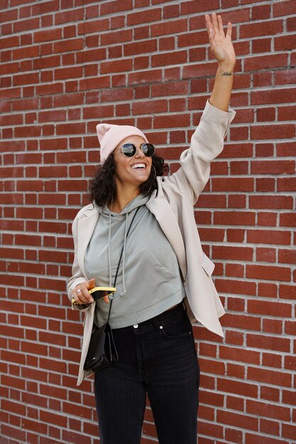 Young stylish woman using smartphone against brick wall in the city