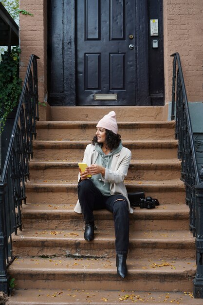 Young stylish woman using smartphone while sitting on steppes in the city