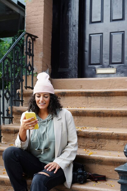 도시의 대초원에 앉아 스마트폰을 사용하는 세련된 젊은 여성