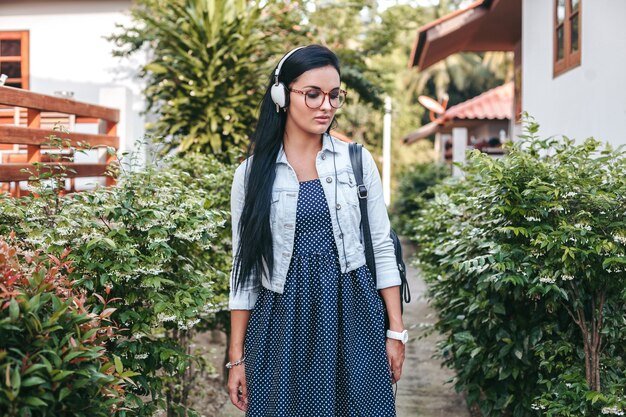 Young stylish woman walking with smartphone, listening to music on headphones, summer vacation