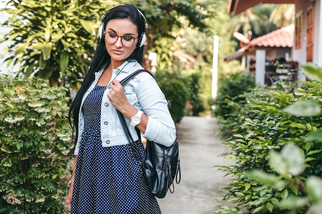 Free photo young stylish woman walking with smartphone, listening to music on headphones, summer vacation