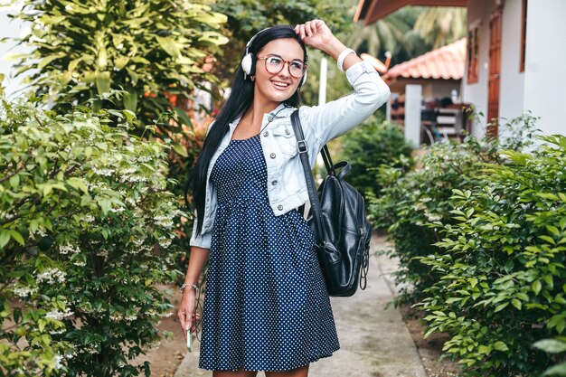 Young stylish woman walking with smartphone, listening to music on headphones, summer vacation