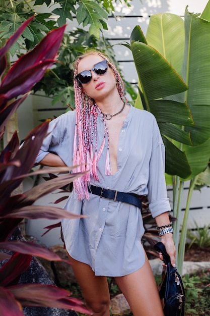 Young stylish woman with pink purple braids and black waist bag posing outdoor