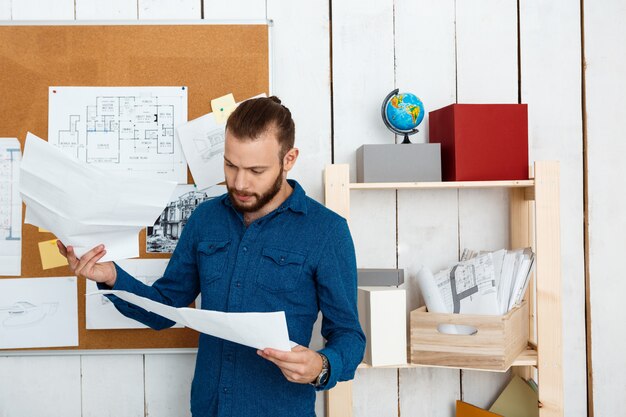Free photo young successful architector looking at drawings, standing in office