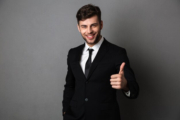 Young successful businessman in formal wear showing thumb up gesture, 