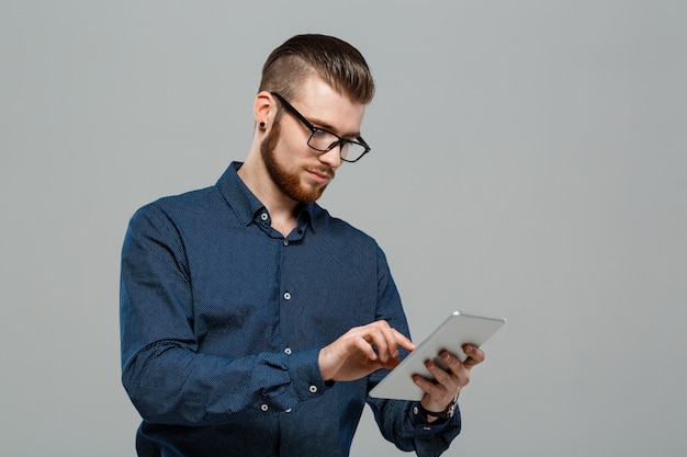 Young successful businessman looking at tablet over grey wall.