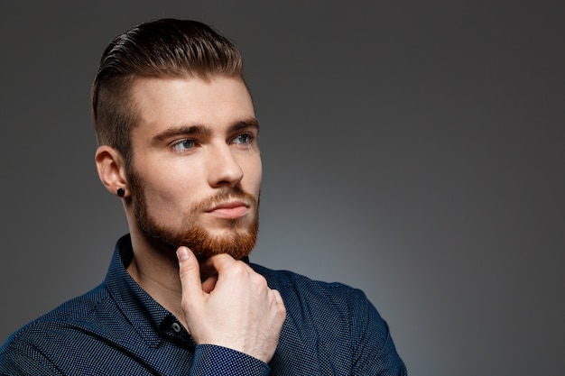 Young successful businessman posing over dark wall.