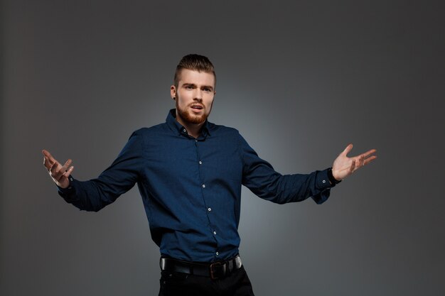 Young successful businessman posing over dark wall.