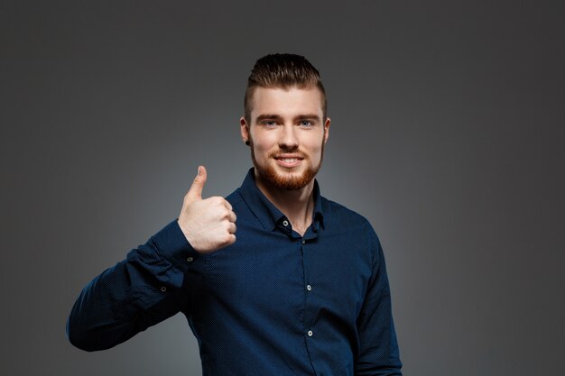 Young successful businessman showing okay over grey wall.