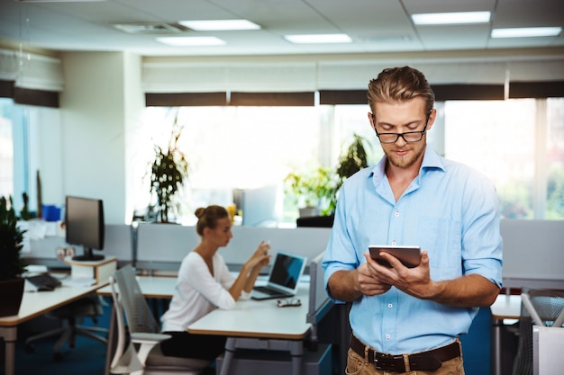 Young successful businessman smiling, looking at tablet, over office
