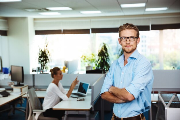 Young successful businessman smiling, posing with crossed arms, over office