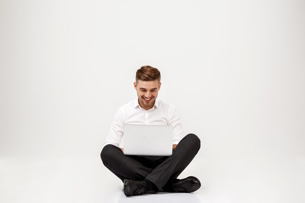 Young successful businessman smiling, sitting with laptop.