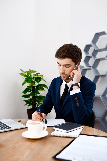 Young successful businessman speaking on phone, office background.