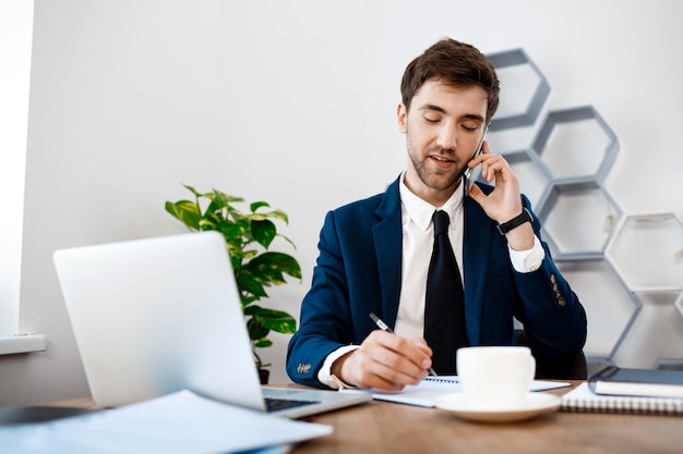 Free photo young successful businessman speaking on phone, office background.