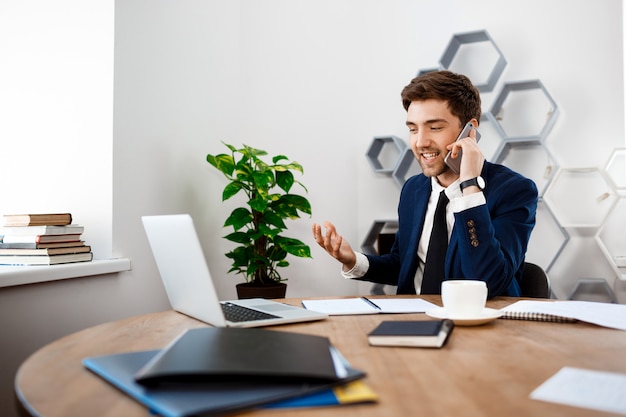 Young successful businessman speaking on phone, office background.